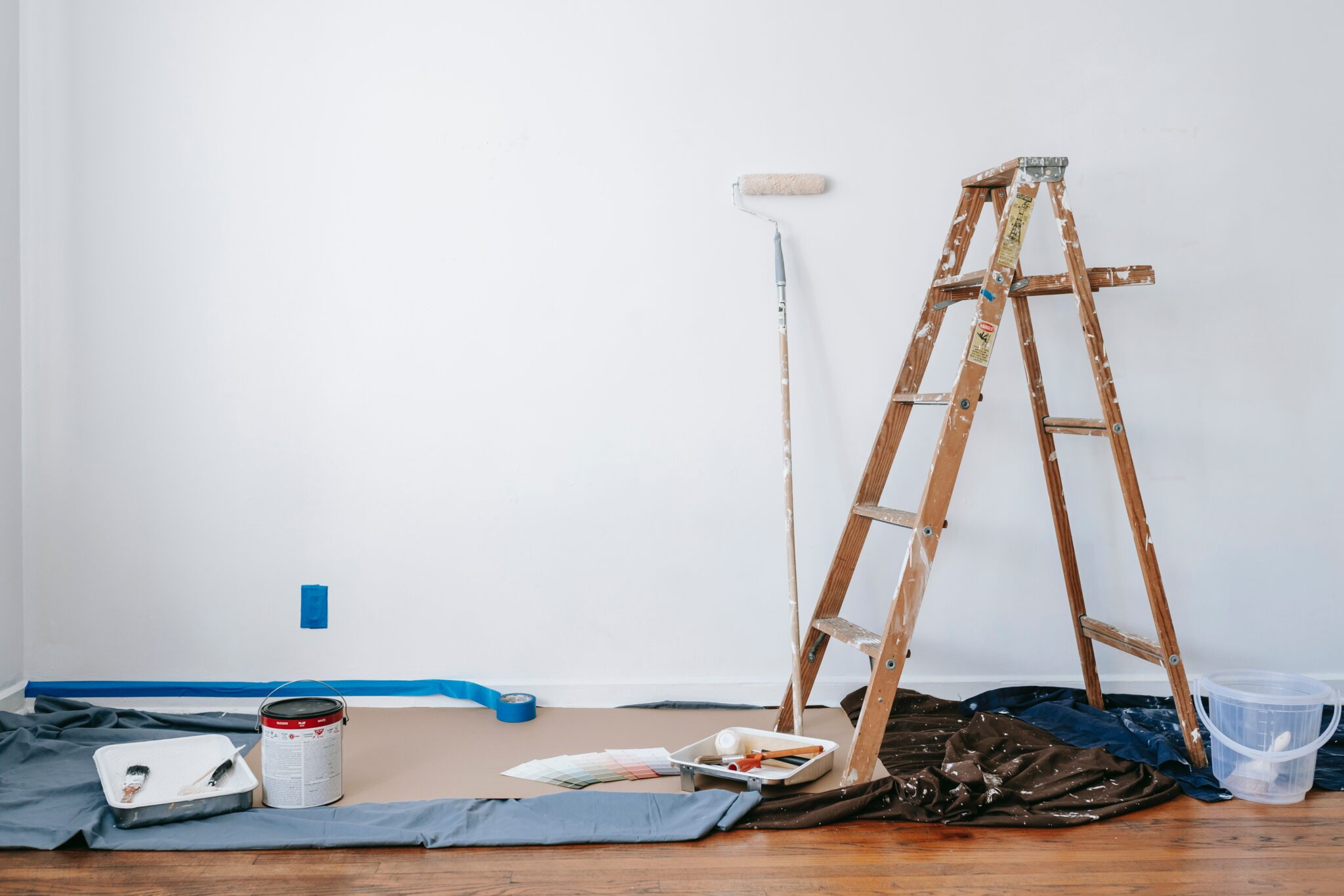 paint brushes, rollers, trays and a step ladder on a drop cloth to paint a room